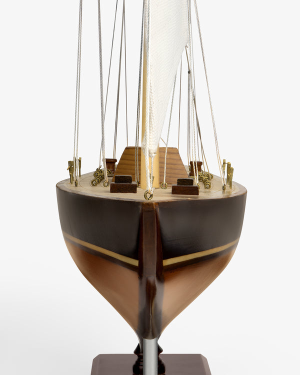 Walnut Model Sailboat seen from the front, showing brown hull, wood deck, mast, sail, and rigging on white background.