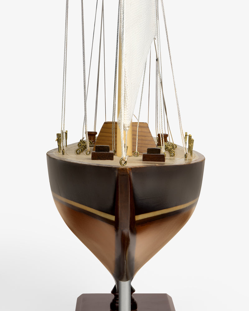 Walnut Model Sailboat seen from the front, showing brown hull, wood deck, mast, sail, and rigging on white background.