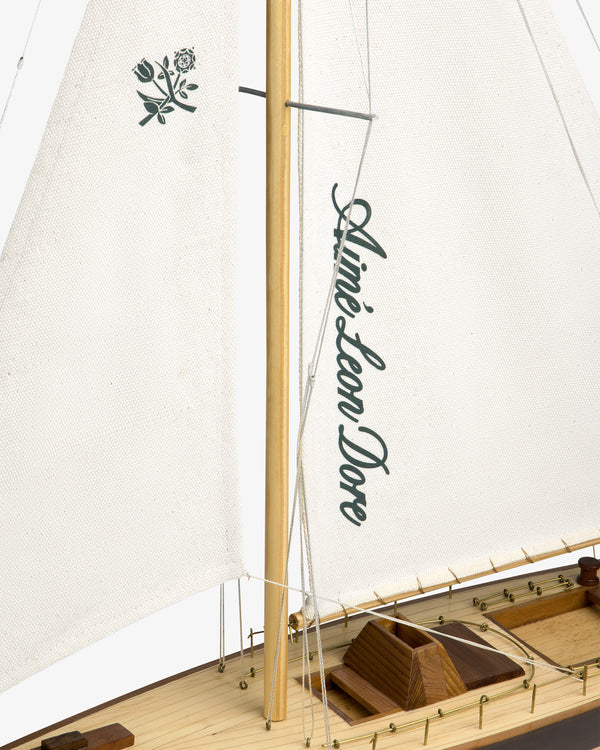 Walnut Model Sailboat with Aimé Leon Dore logo and rose emblem on white sails, featuring a visible wooden deck.