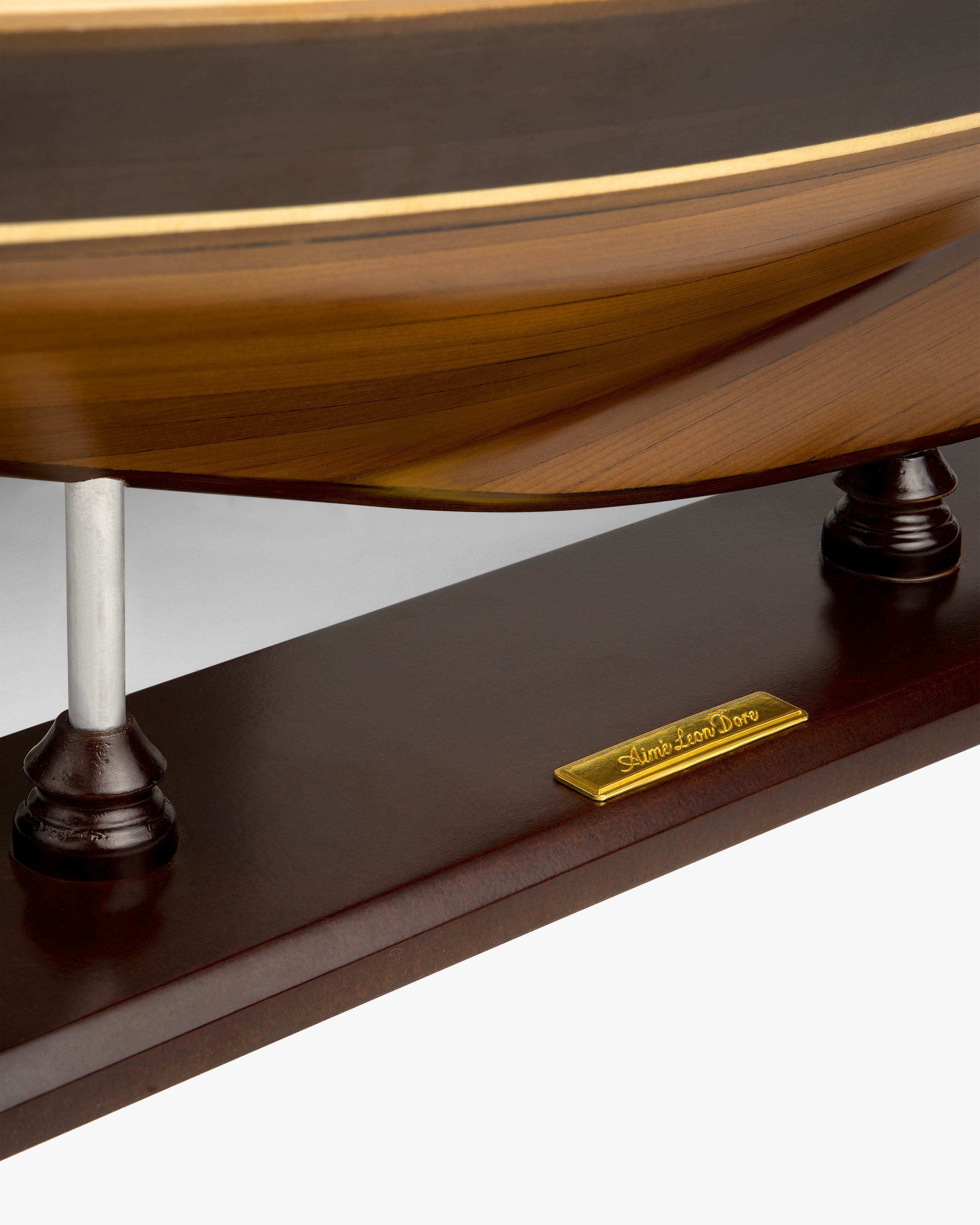 Close-up of a Walnut Model Sailboat’s base with a gold nameplate that reads “Walnut Model Sailboat.”.