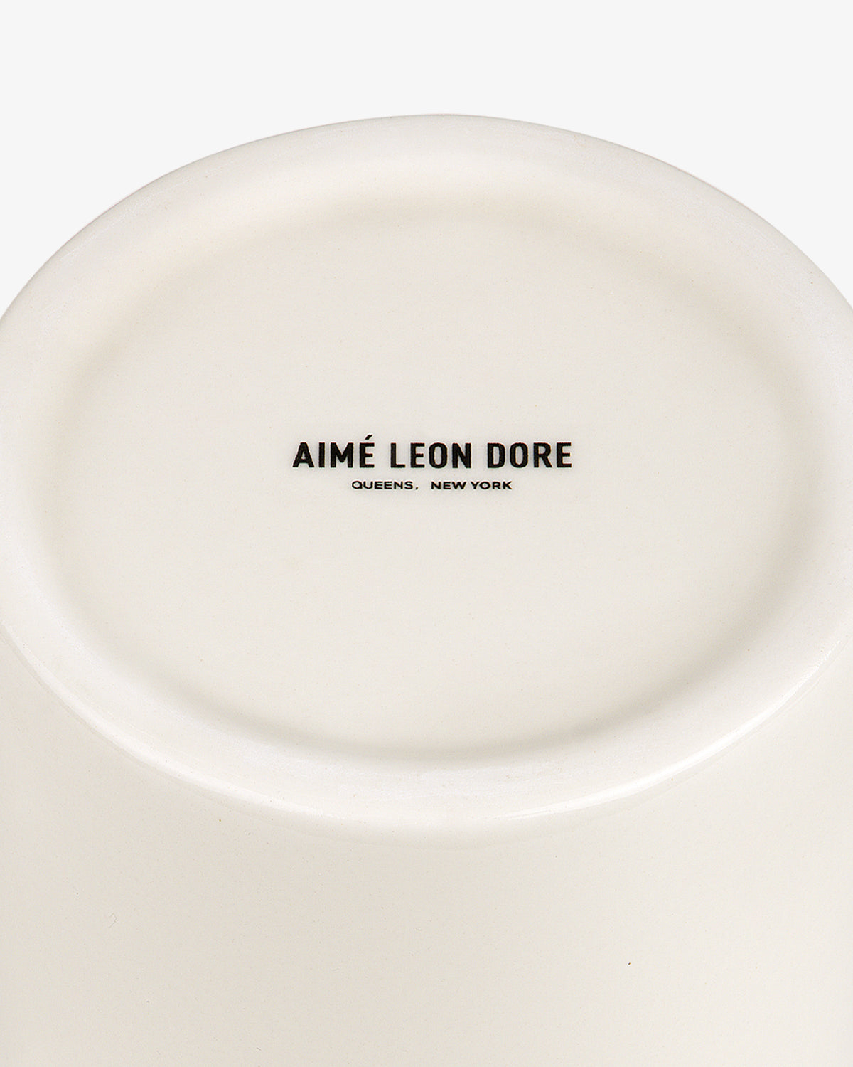 The bottom of a white Krylon Ceramic Spray Can Vessel with AIMÉ LEON DORE QUEENS, NEW YORK printed in black.