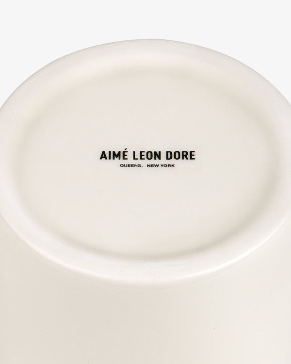 The bottom of a white Krylon Ceramic Spray Can Vessel with AIMÉ LEON DORE QUEENS, NEW YORK printed in black.
