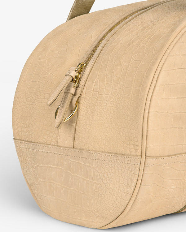 The Croc-Embossed Nubuck Duffle is a beige handbag with crocodile texture, gold zipper, and curved design.