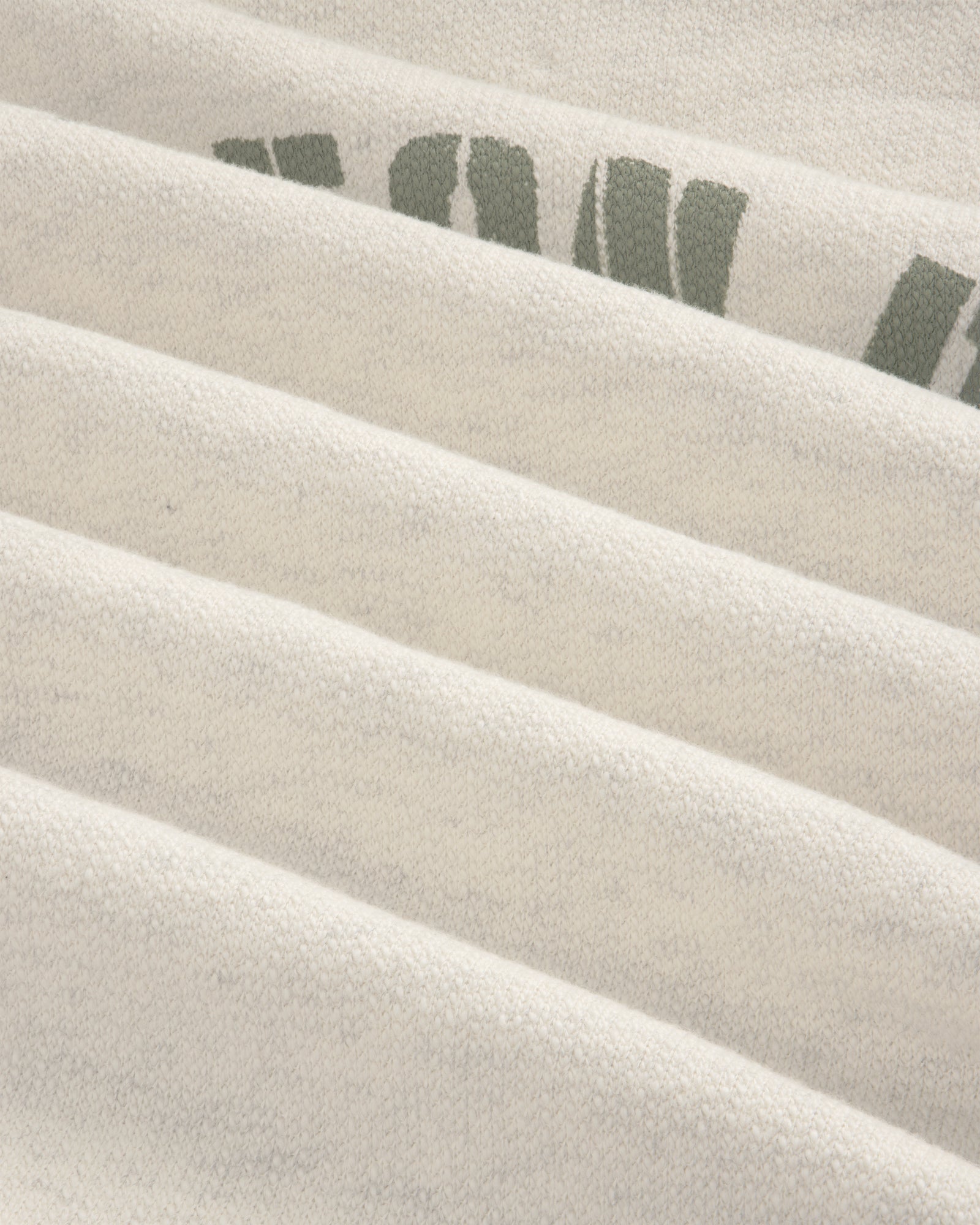 Close-up of folded Dock Hoodie in light gray with partial green letters on the top right fold.