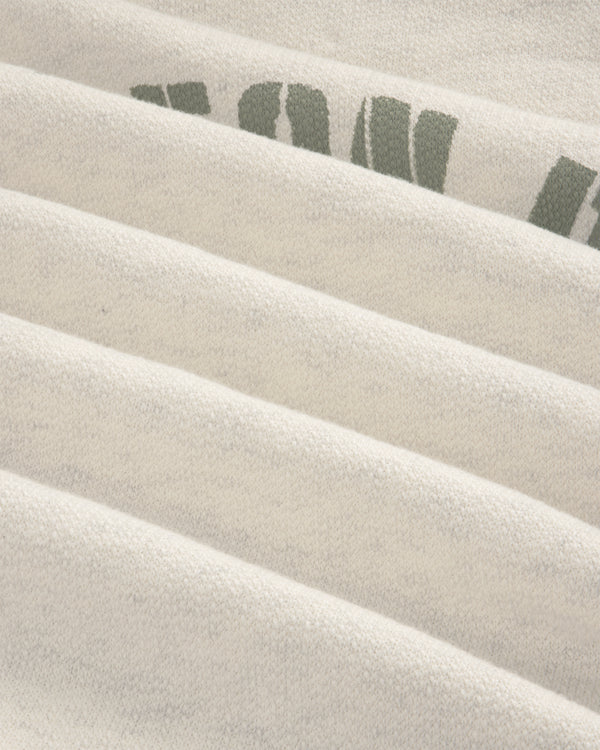 Close-up of folded Dock Hoodie in light gray with partial green letters on the top right fold.
