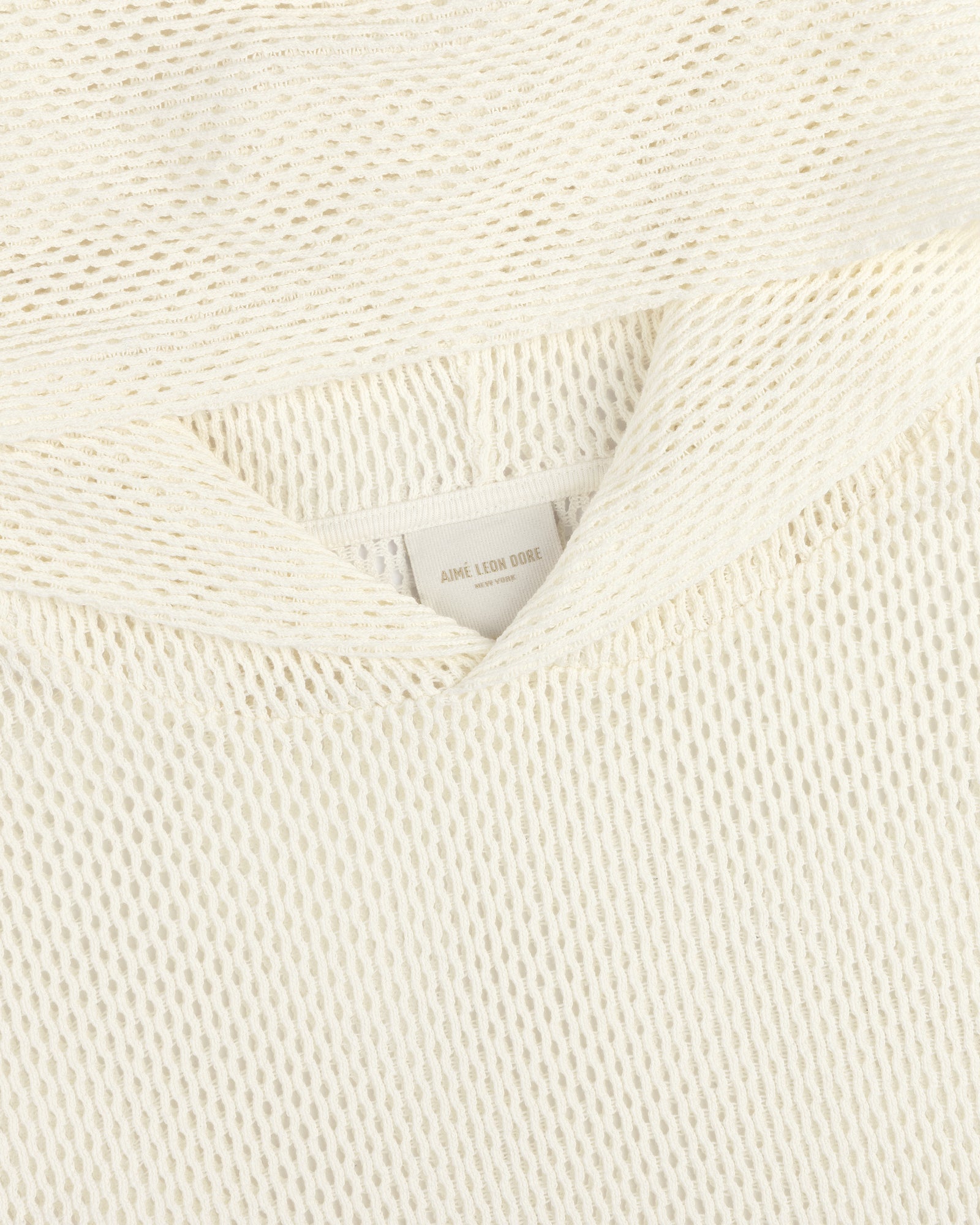 Close-up of a cream-colored open mesh hoodie with a textured knit and a visible AIMÉ LEON DORE label.