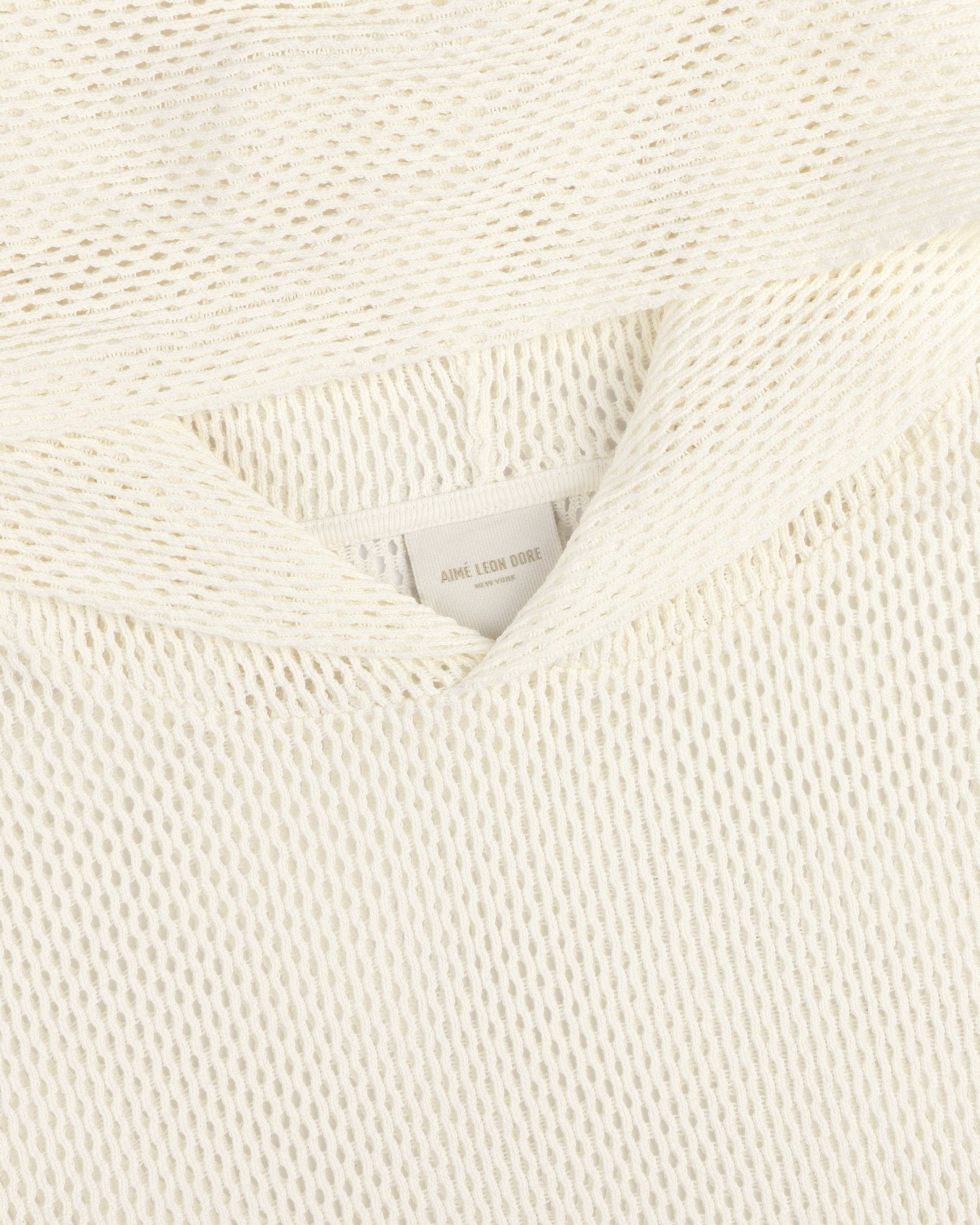 Close-up of a cream-colored open mesh hoodie with a textured knit and a visible AIMÉ LEON DORE label.