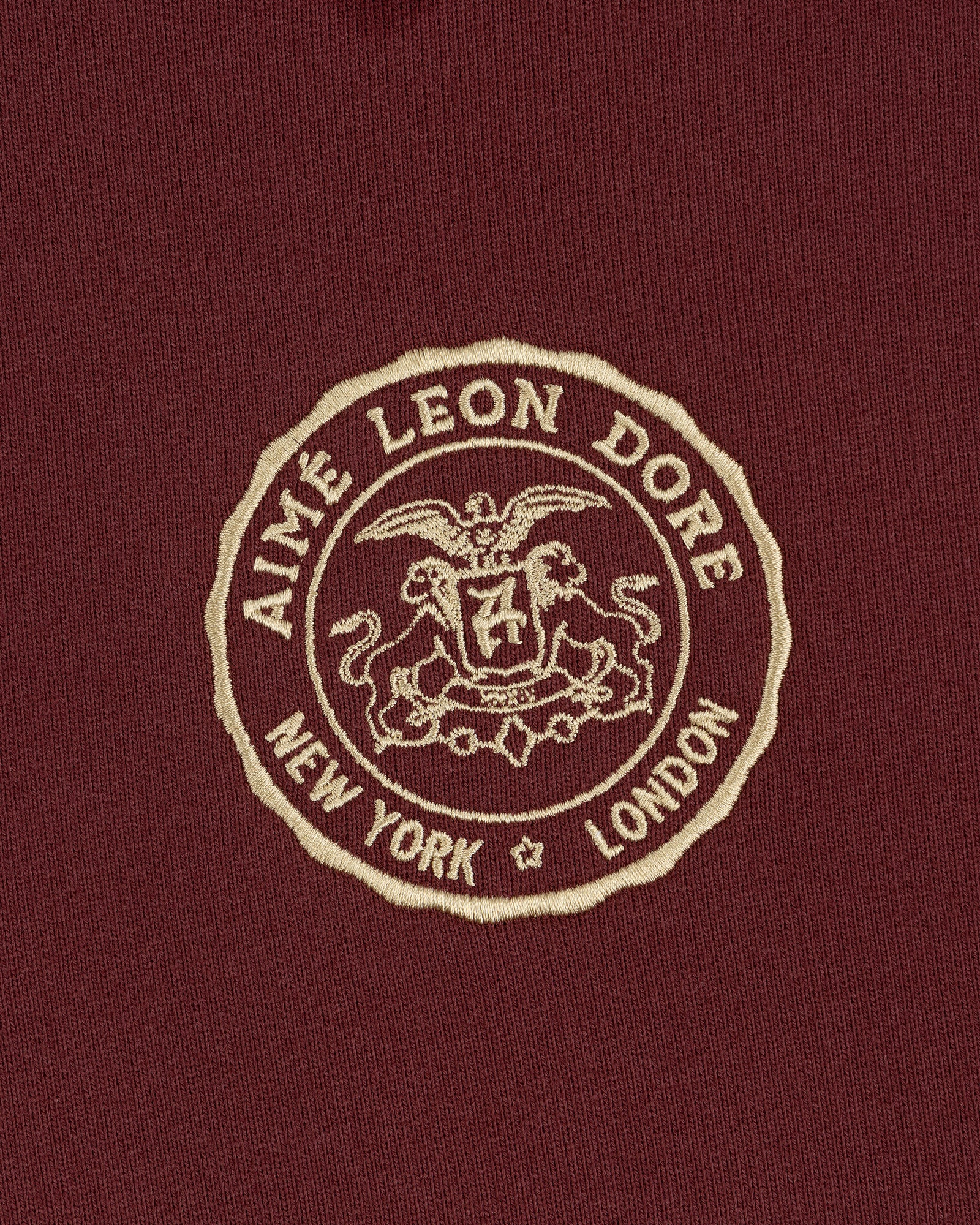 Embroidered Aimé Leon Dore crest with eagle, shield, and "New York London" on maroon Signet Logo Hoodie.
