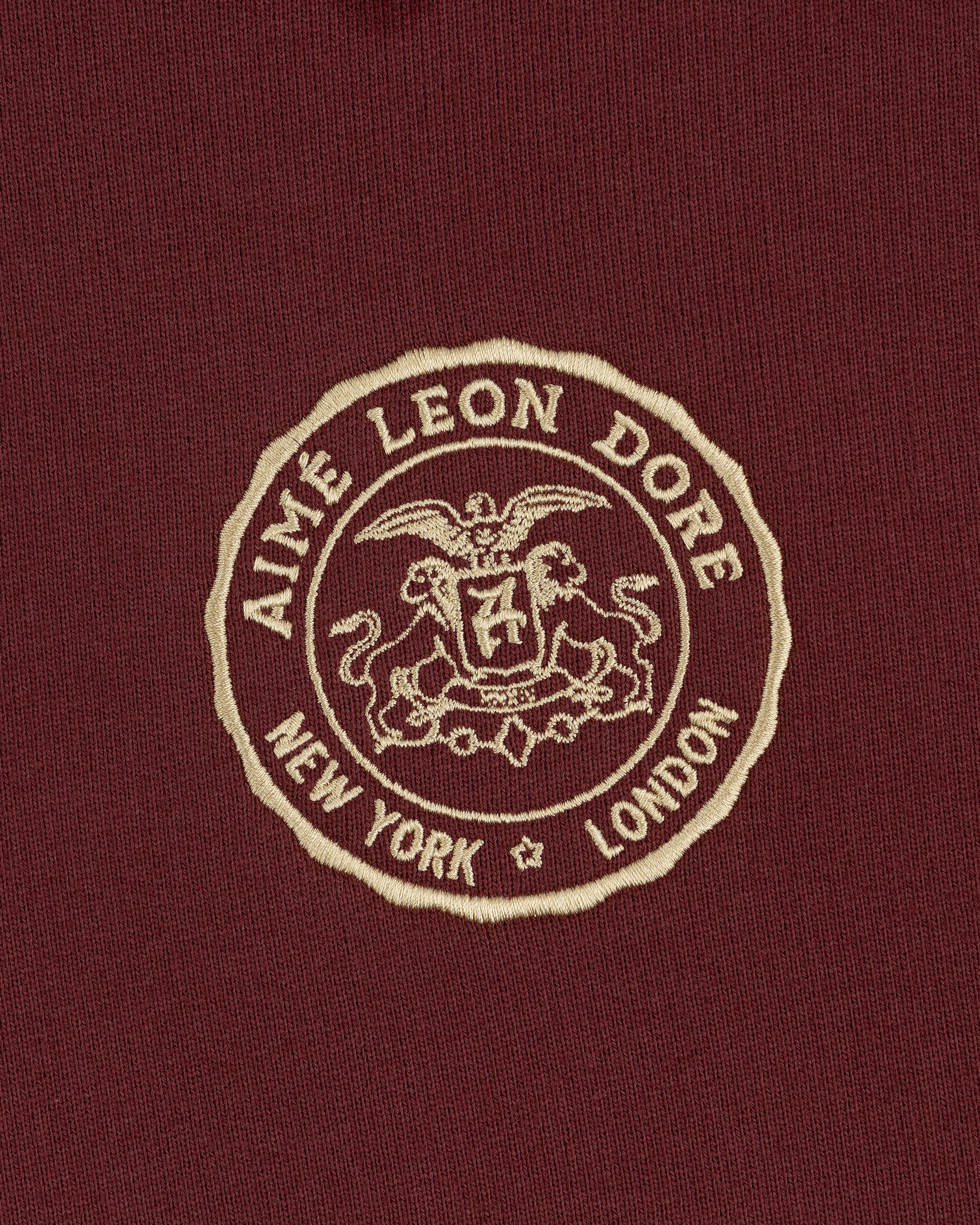 Embroidered Aimé Leon Dore crest with eagle, shield, and "New York London" on maroon Signet Logo Hoodie.