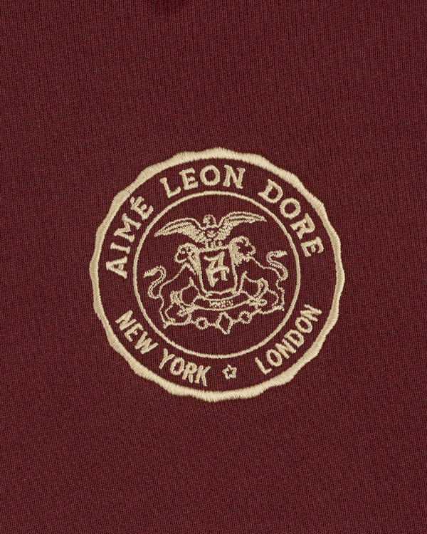 Embroidered Aimé Leon Dore crest with eagle, shield, and "New York London" on maroon Signet Logo Hoodie.