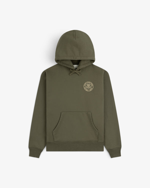 Signet Logo Hoodie in olive green with front pocket and small gold circular emblem on the left chest.