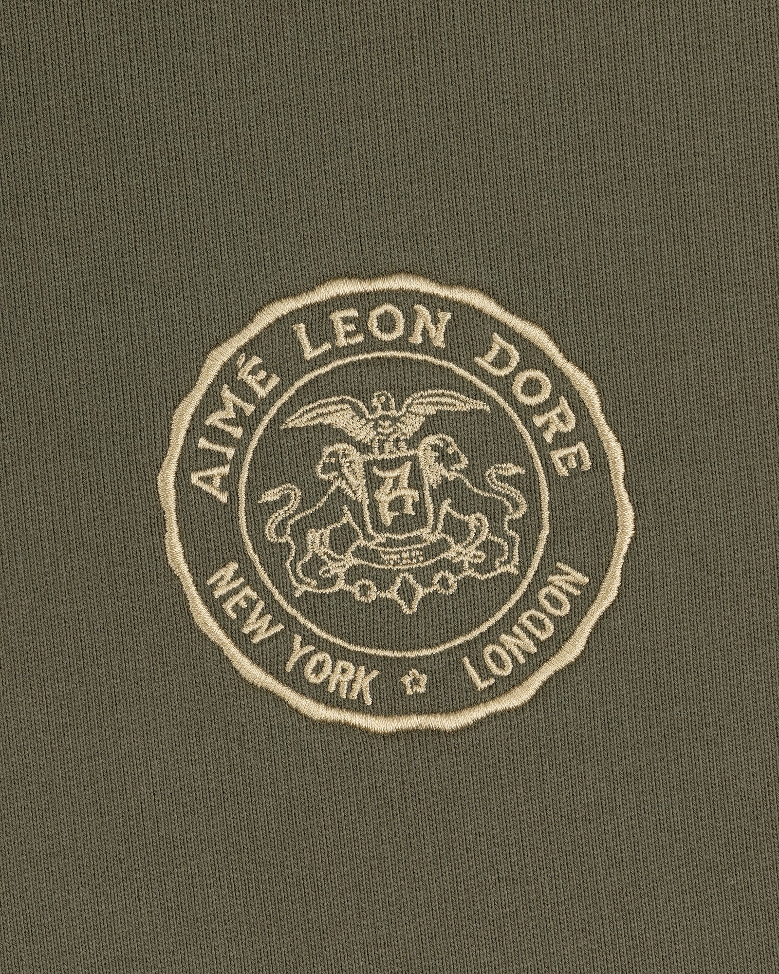 Signet Logo Hoodie featuring an embroidered Aimé Leon Dore crest with New York and London on olive green fabric.