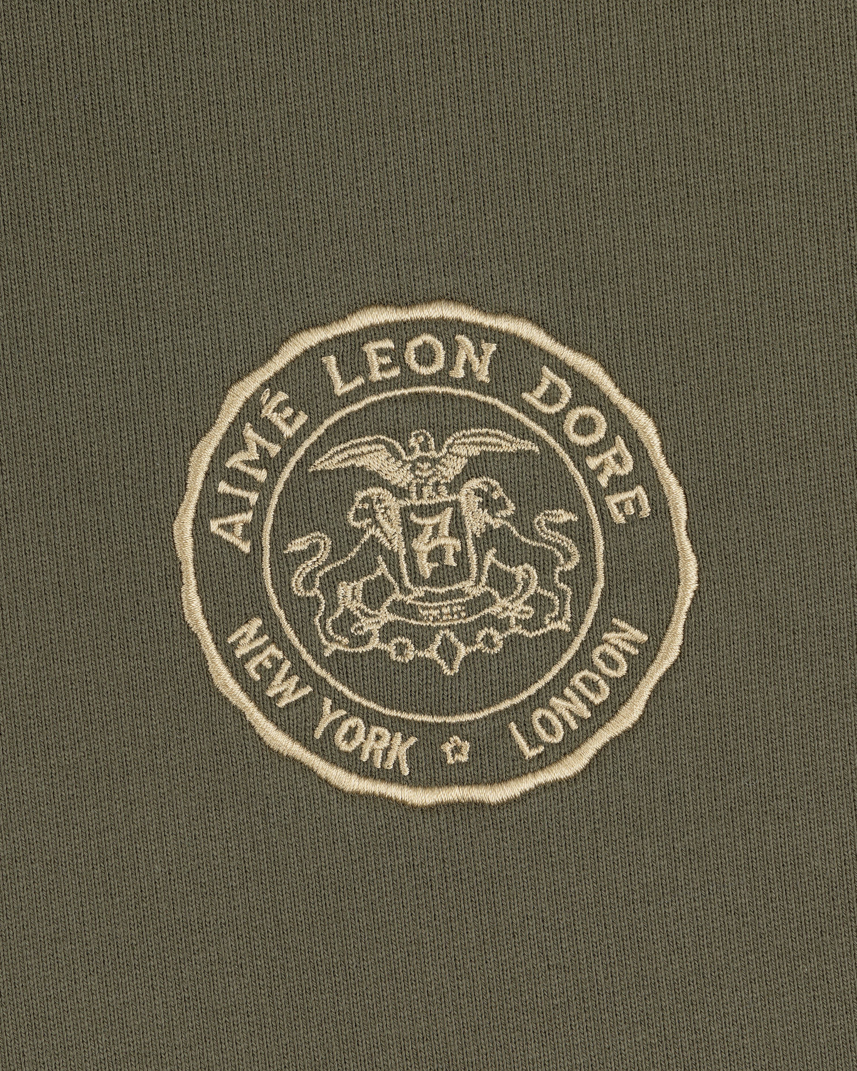 Signet Logo Hoodie featuring an embroidered Aimé Leon Dore crest with New York and London on olive green fabric.