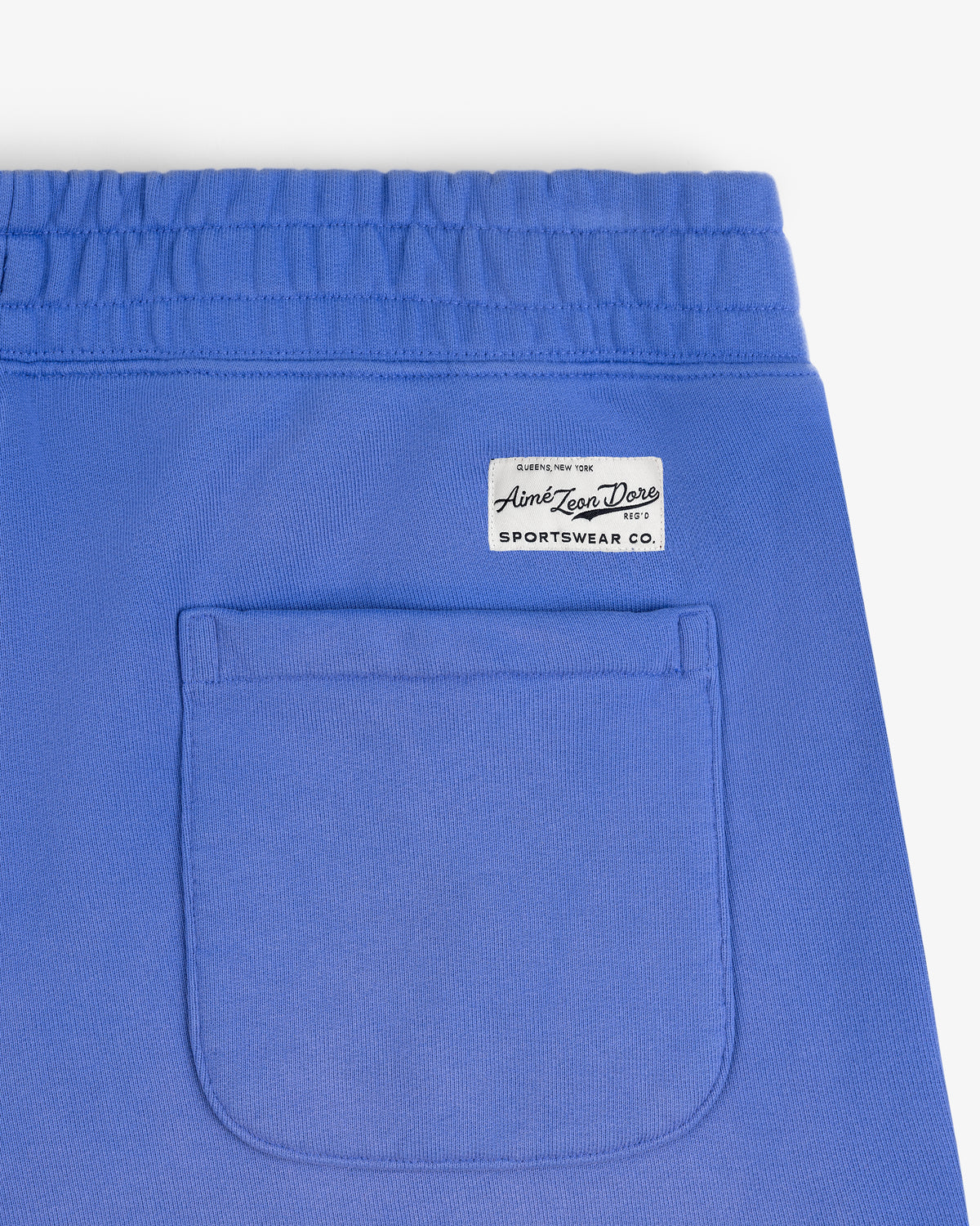 Close-up of Sun Faded Sweatpants in blue with an elastic waistband, patch pocket, and white Aime Leon Dore label.