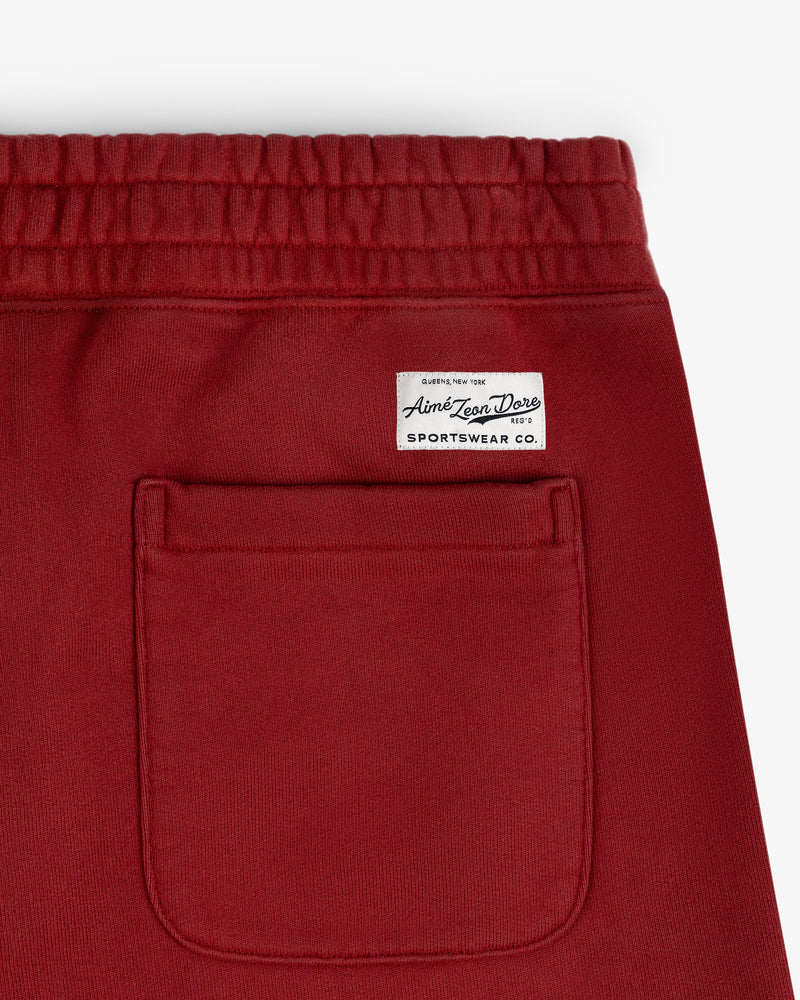 Close-up of Sun Faded Sweatpants in red with a back pocket and a white sewn Aime Leon Dore Sportswear Co. label.