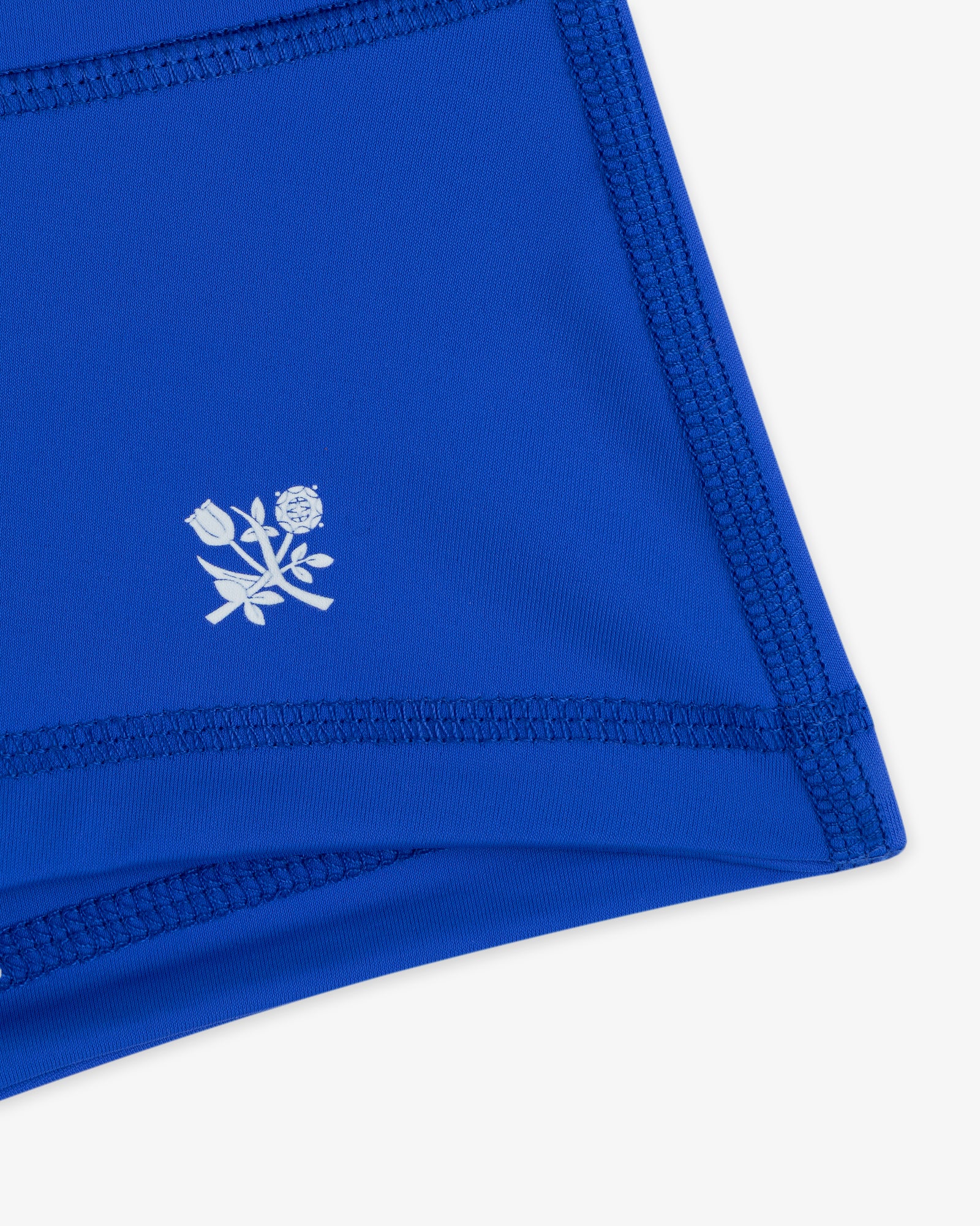 Close-up of Crest Swim Short in blue, featuring dark stitching and a small white floral emblem.