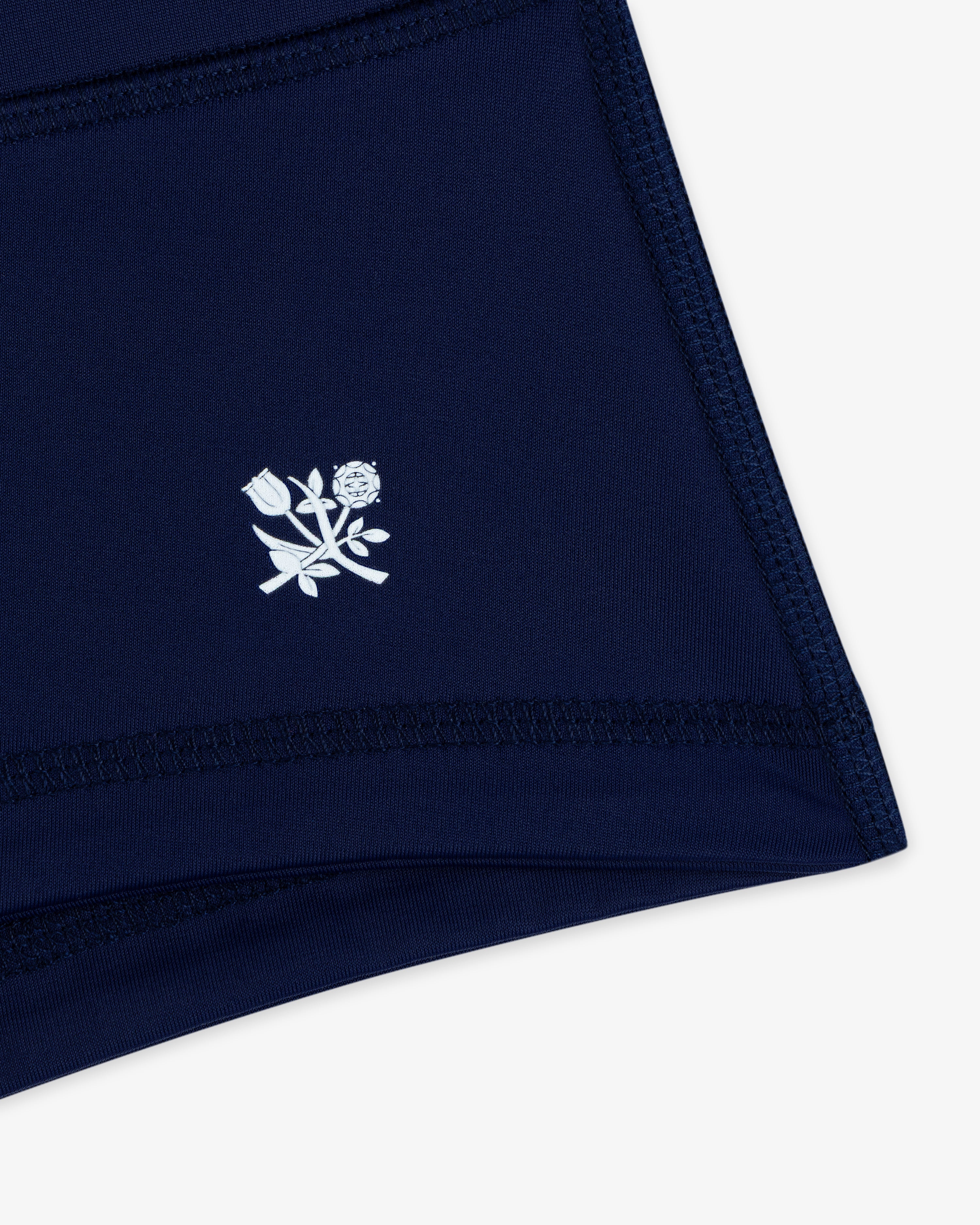 Close-up of Crest Swim Short in navy blue with a small white floral emblem near the hem.