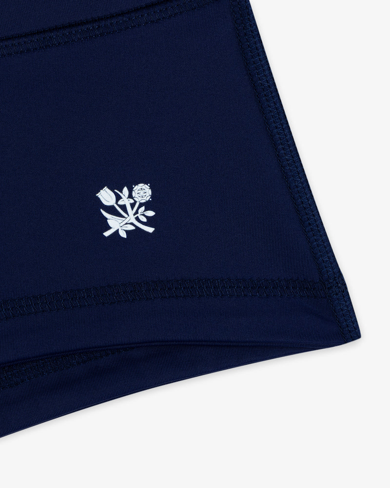 Close-up of Crest Swim Short in navy blue with a small white floral emblem near the hem.