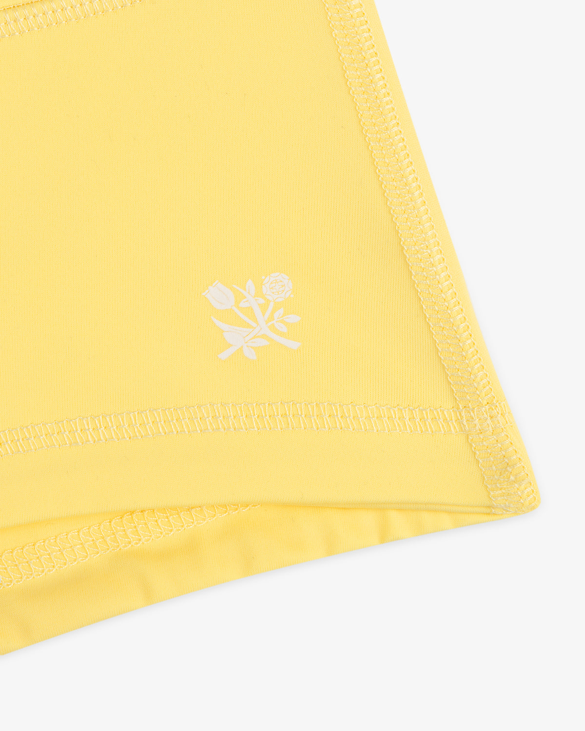 Close-up of Crest Swim Short’s yellow fabric with zigzag stitching and a small white floral print near the edge.
