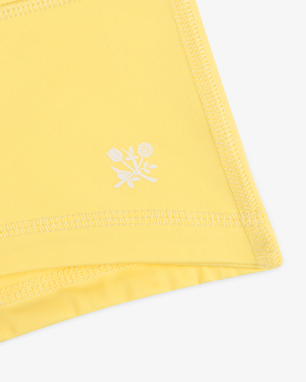 Close-up of Crest Swim Short’s yellow fabric with zigzag stitching and a small white floral print near the edge.