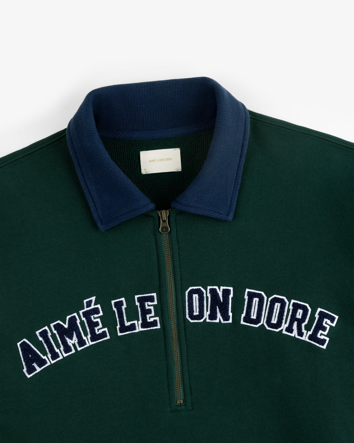 The Collegiate Quarter Zip Pullover is dark green with a navy collar and "AIMÉ LEON DORE" in white on the chest.