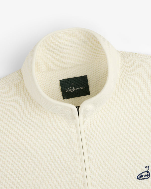 Close-up of the ALD Golf Piqué Full Zip Sweater with a ribbed texture and small navy Aimé Leon Dore chest logo.