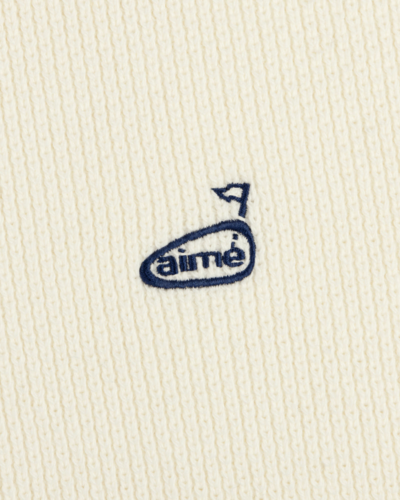 Close-up of the ALD Golf Piqué Full Zip Sweater with a cream knit and small blue embroidered aimé logo with an arrow.