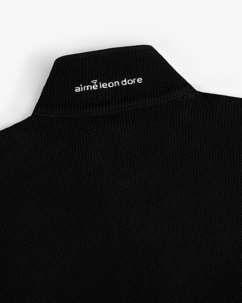 Close-up of the black ribbed collar on the ALD Golf Piqué Full Zip Sweater with white aime leon dore text on the back.