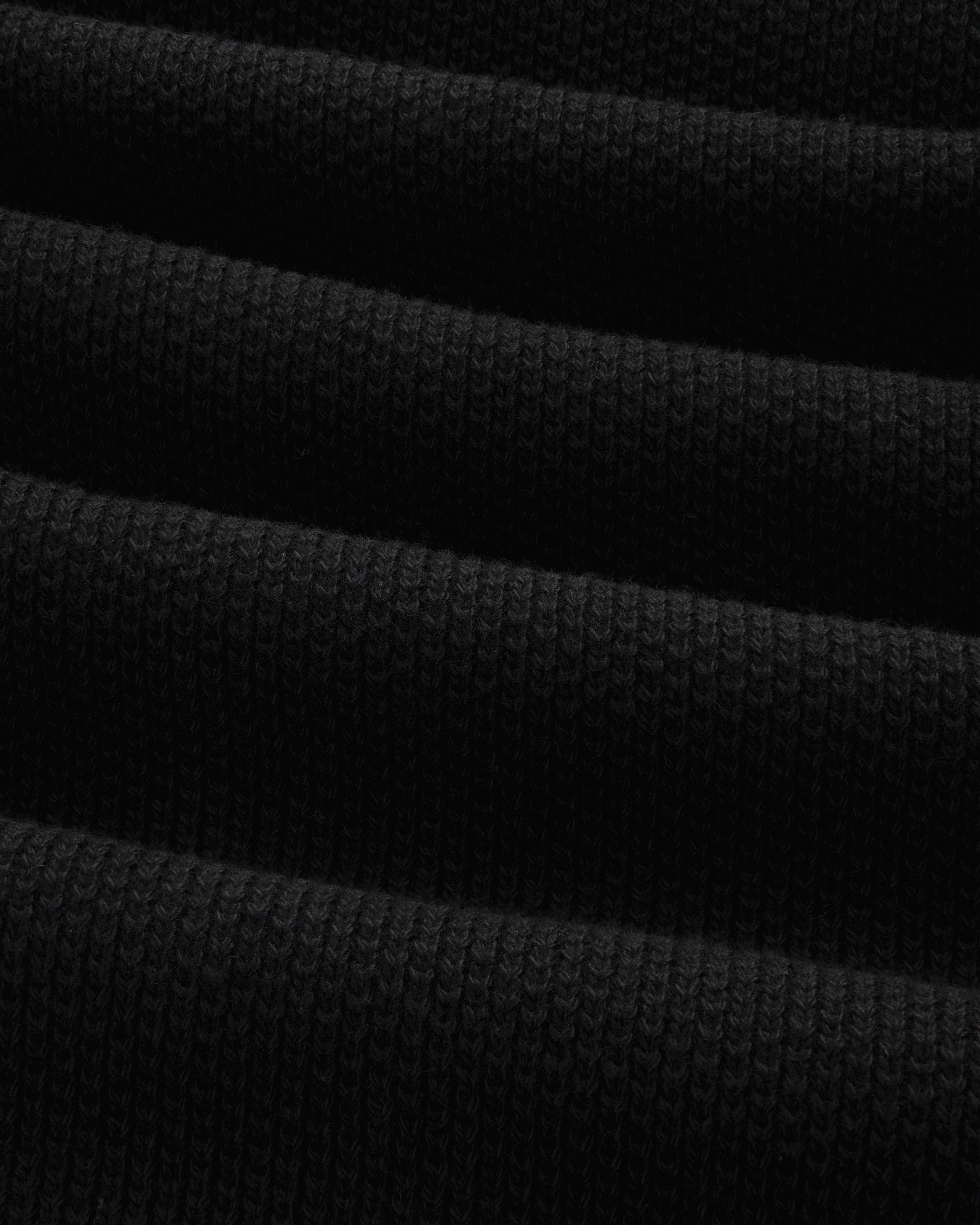 Close-up of ALD Golf Piqué Full Zip Sweater in black, showing ribbed fabric with horizontal folds and textured knit.