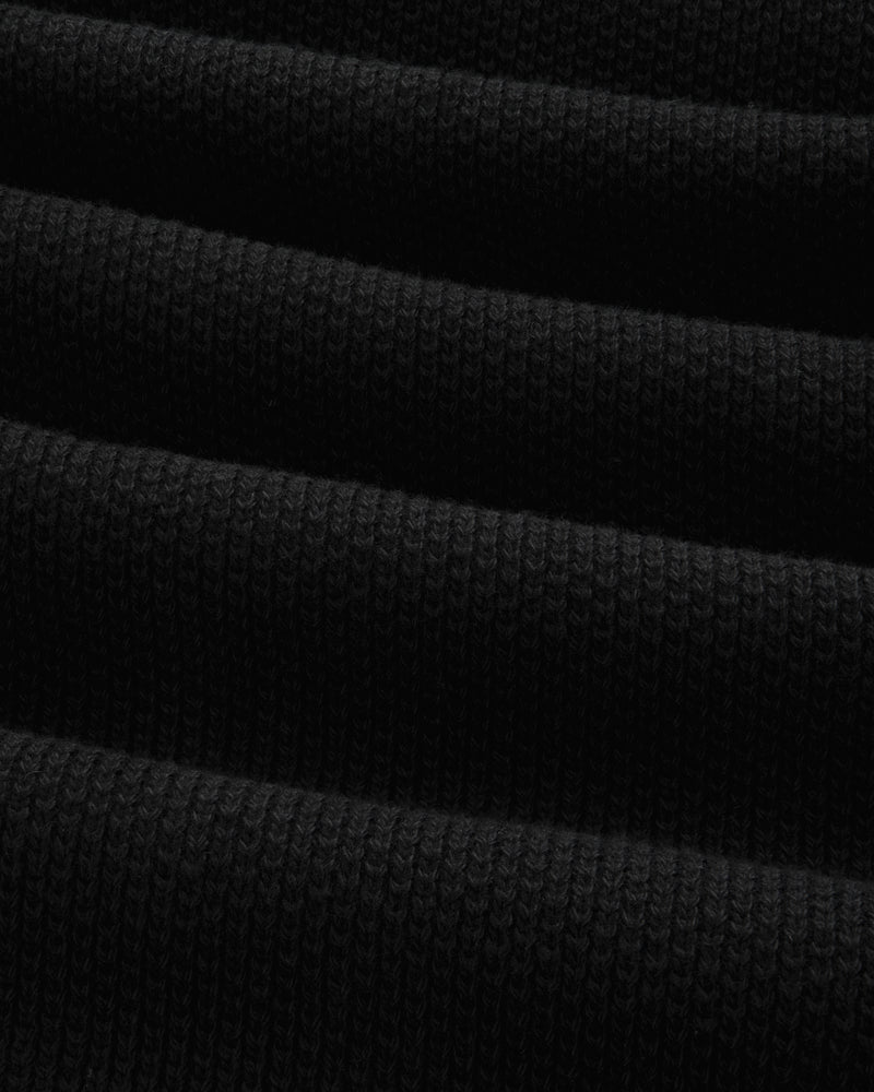 Close-up of ALD Golf Piqué Full Zip Sweater in black, showing ribbed fabric with horizontal folds and textured knit.