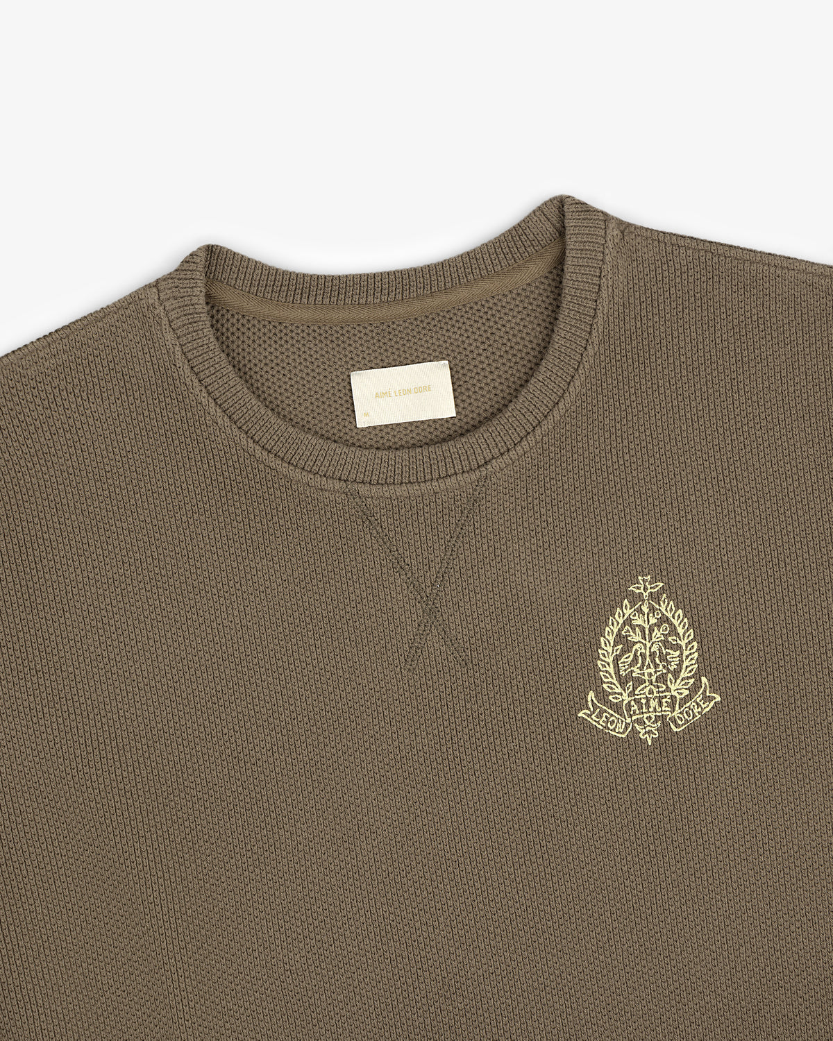 Saint George Piqué Crewneck Sweatshirt in olive green with a yellow chest crest and visible interior label.