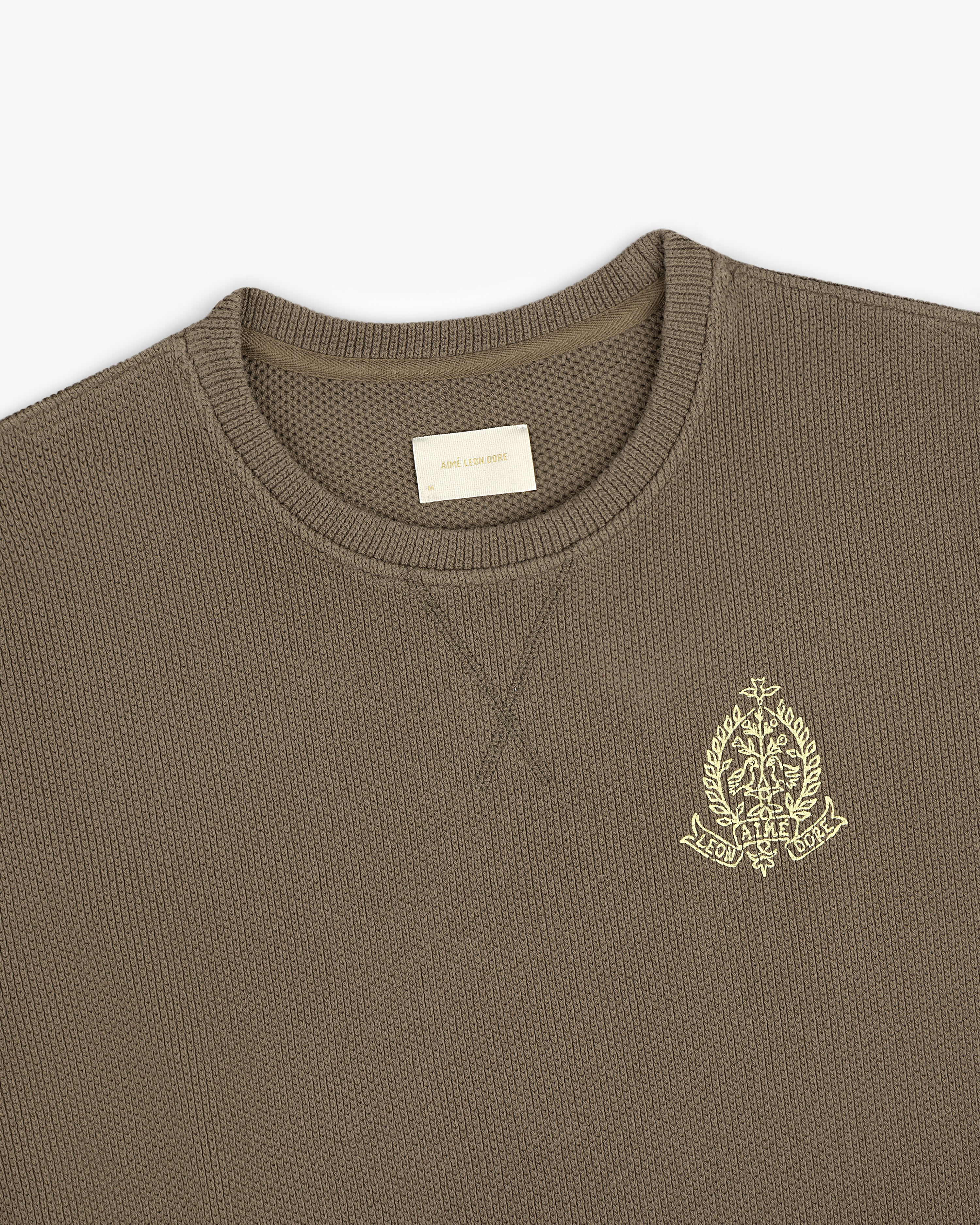 Saint George Piqué Crewneck Sweatshirt in olive green with a yellow chest crest and visible interior label.