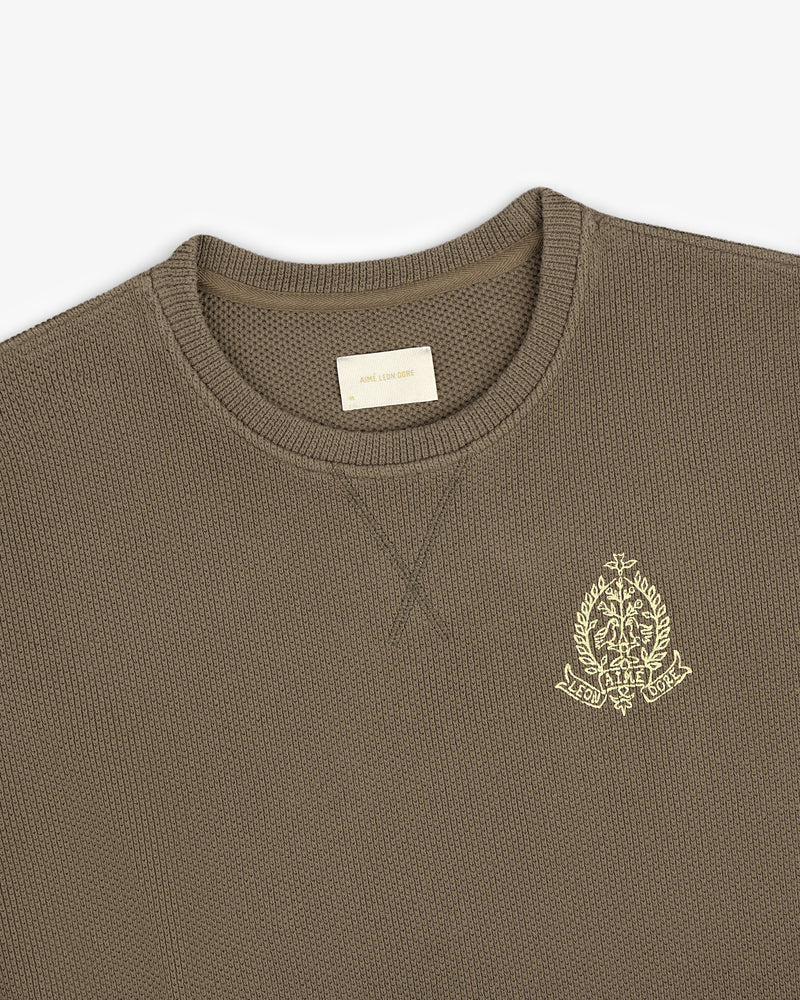 Saint George Piqué Crewneck Sweatshirt in olive green with a yellow chest crest and visible interior label.
