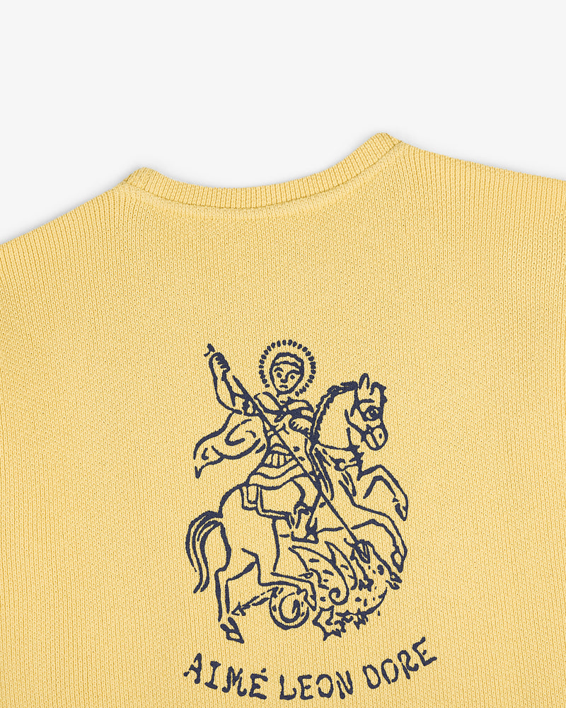 Yellow knit Saint George Piqué Crewneck with navy knight slaying dragon graphic and AIMÉ LEON DORE text below.