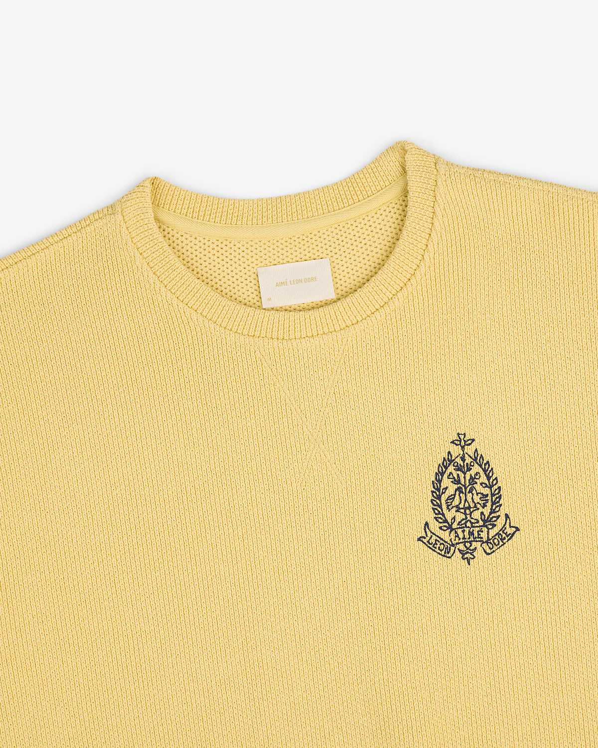Saint George Piqué Crewneck Sweatshirt in yellow with a navy crest on the left chest and beige collar tag.