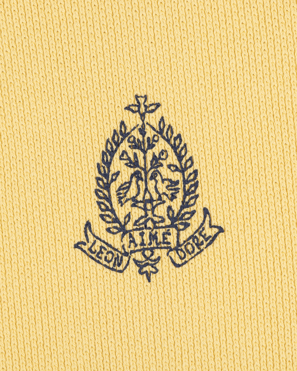 Saint George Piqué Crewneck Sweatshirt with navy crest, two birds, and AIME LEON DORE text on yellow knit fabric.