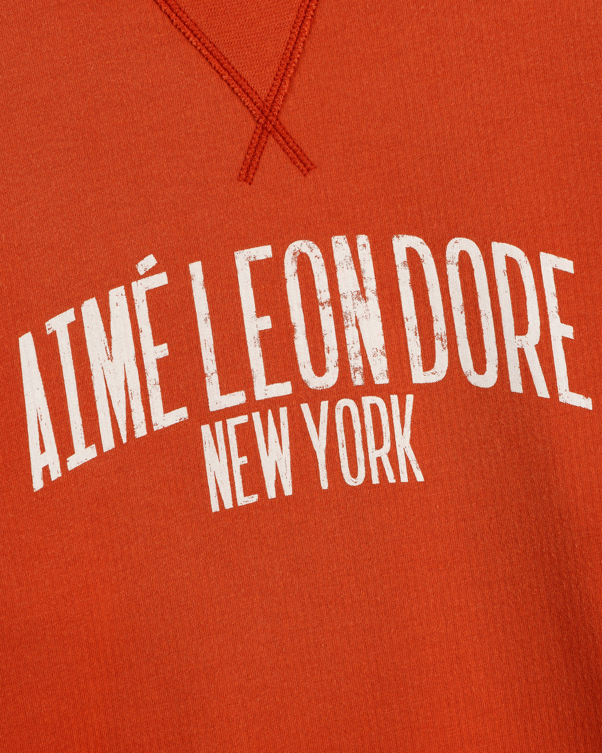 Close-up of orange Vintage Washed Crewneck Sweatshirt with white AIMÉ LEON DORE NEW YORK text in a curved font.