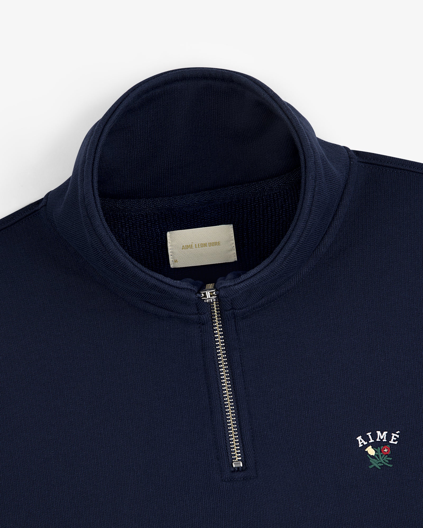 Crest Quarter Zip Pullover in navy with AIMÉ and a red rose embroidered on the chest.