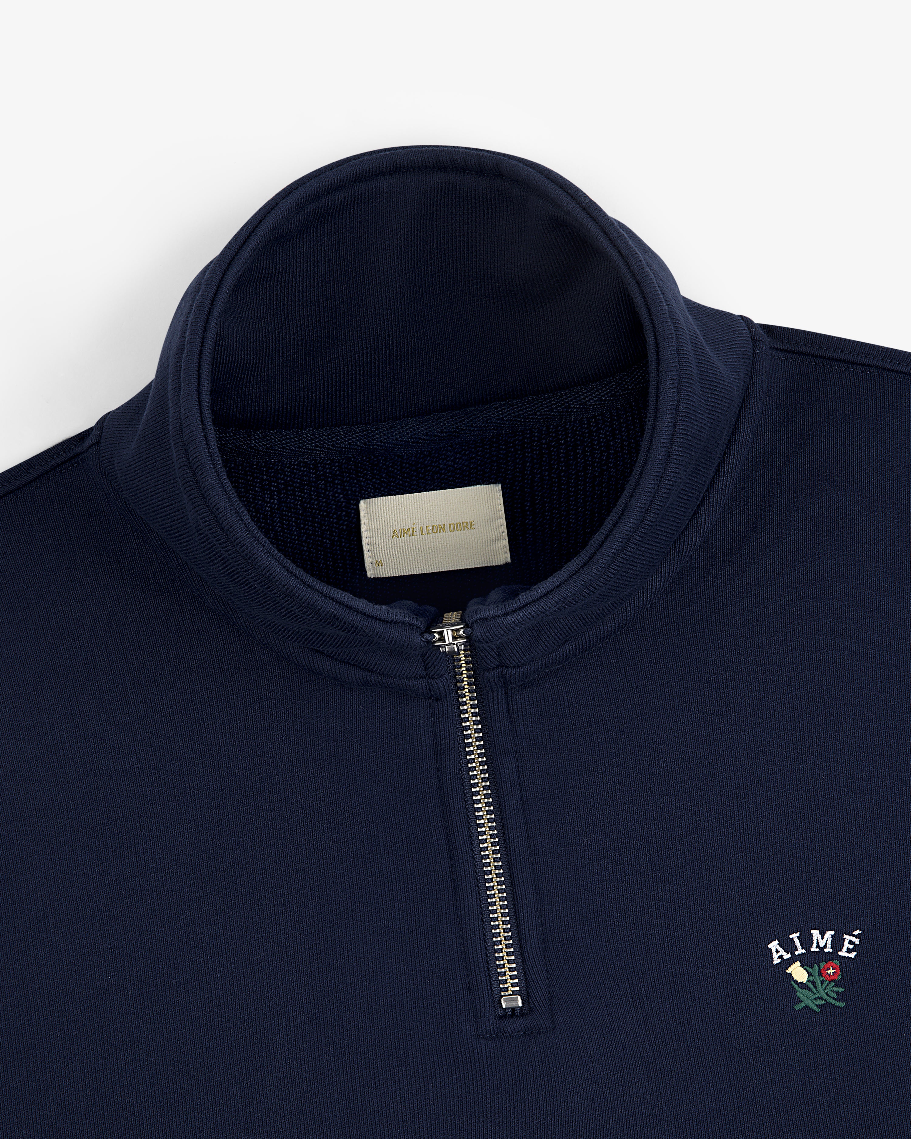 Crest Quarter Zip Pullover in navy with AIMÉ and a red rose embroidered on the chest.
