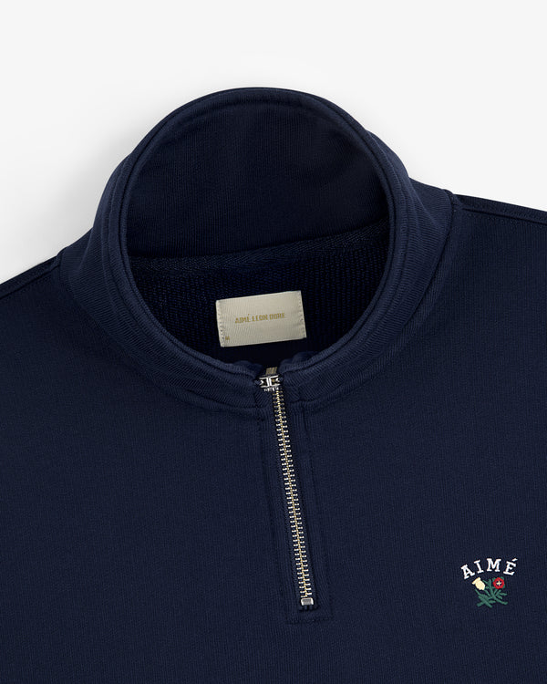 Crest Quarter Zip Pullover in navy with AIMÉ and a red rose embroidered on the chest.