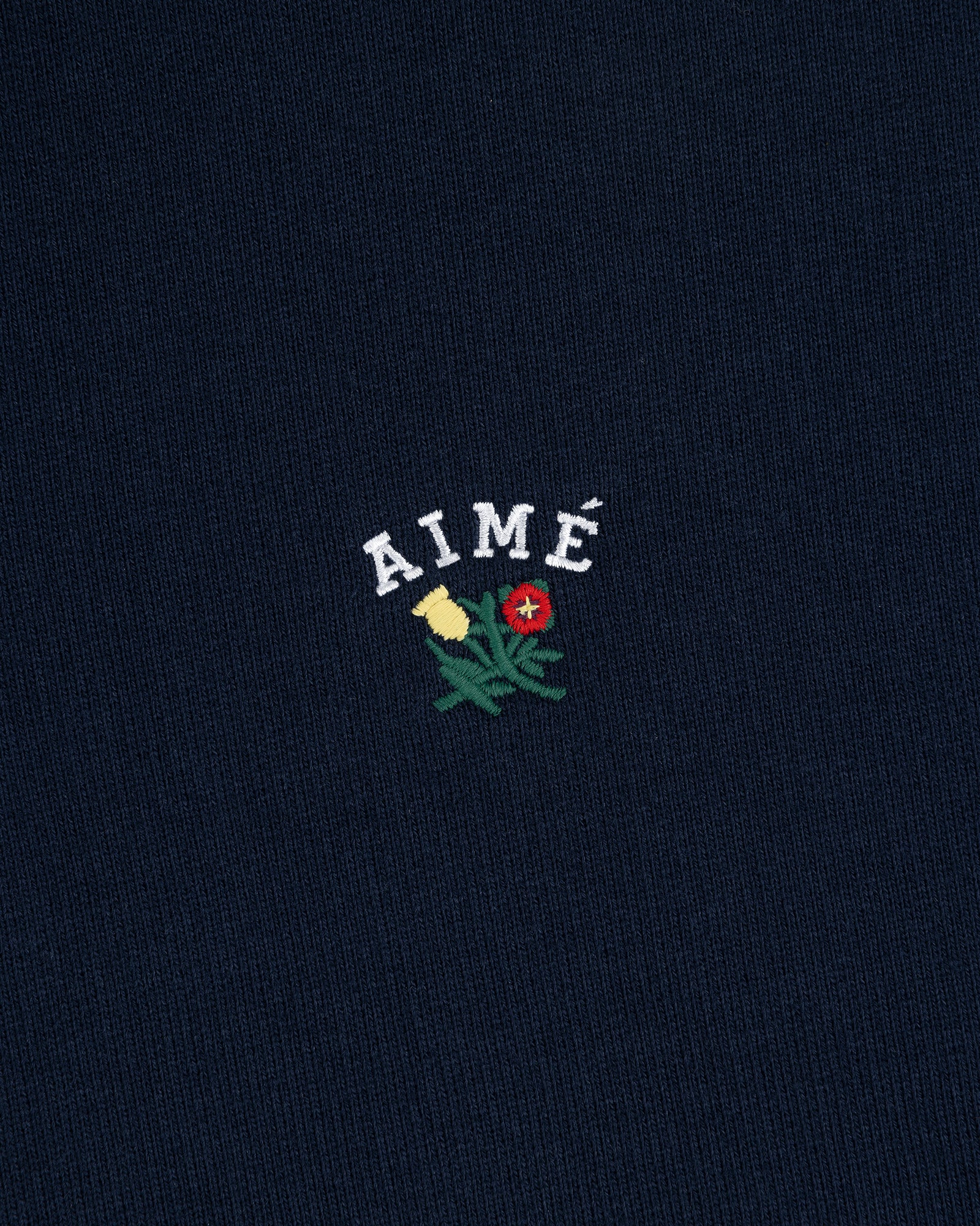 Navy blue Crest Quarter Zip Pullover with AIMÉ embroidered above a yellow and red flower with green stems.