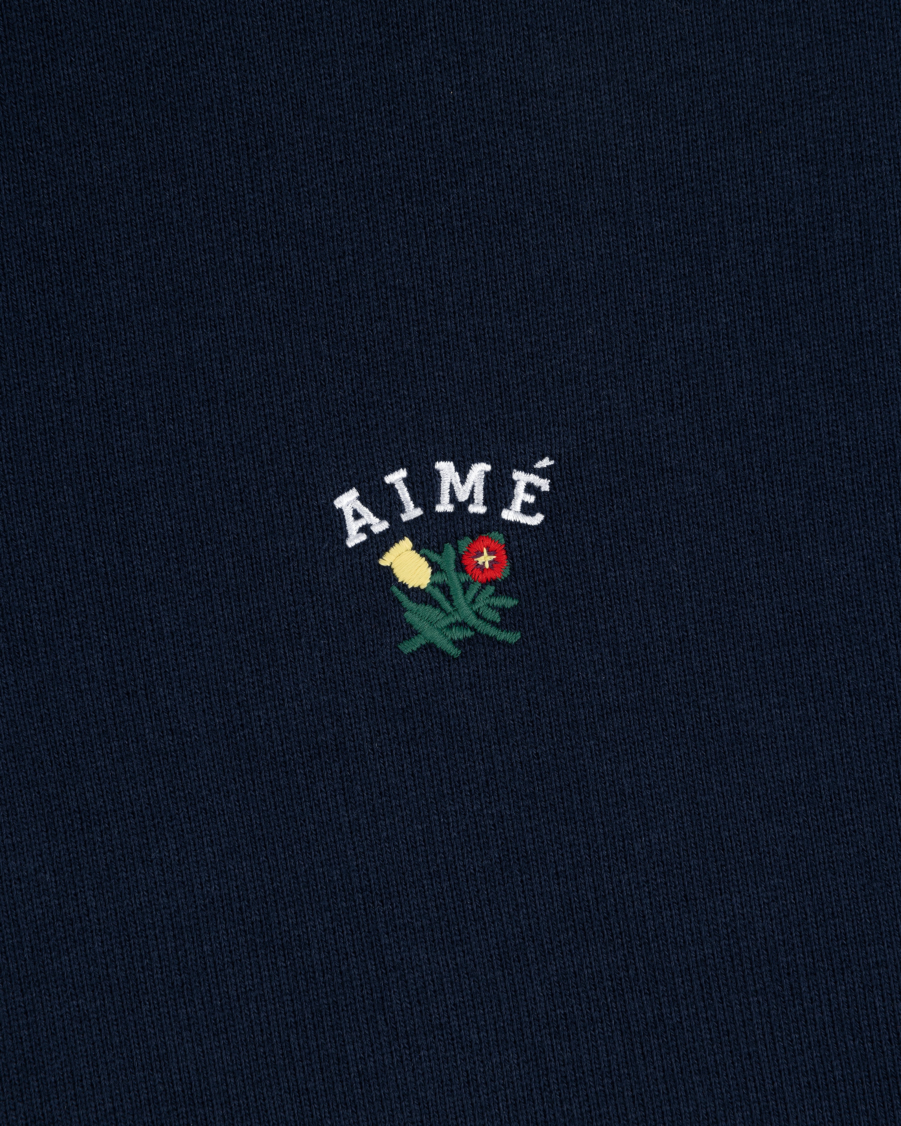Navy blue Crest Quarter Zip Pullover with AIMÉ embroidered above a yellow and red flower with green stems.