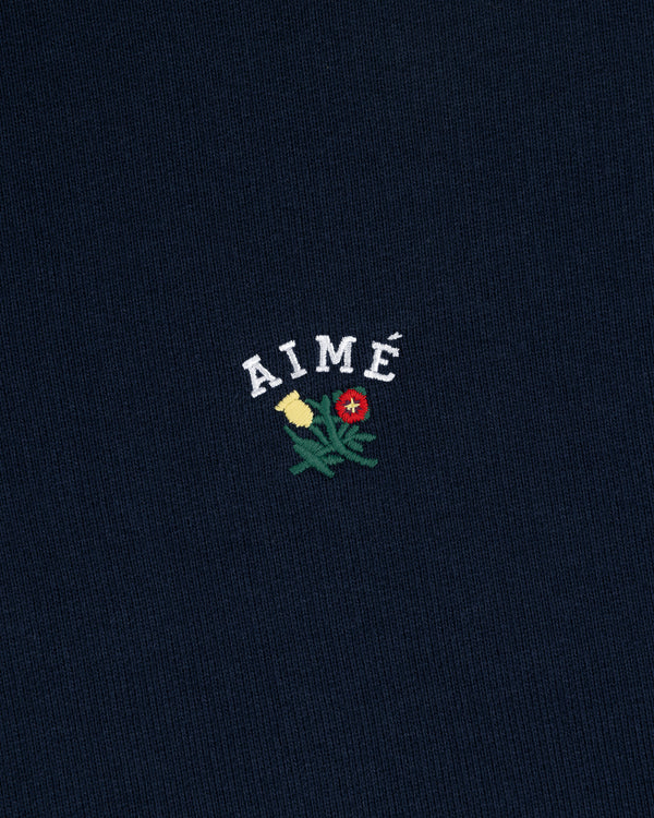 Navy blue Crest Quarter Zip Pullover with AIMÉ embroidered above a yellow and red flower with green stems.