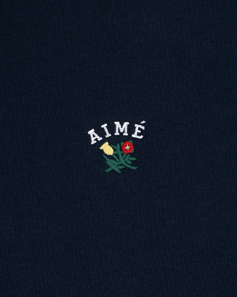 Navy blue Crest Quarter Zip Pullover with AIMÉ embroidered above a yellow and red flower with green stems.