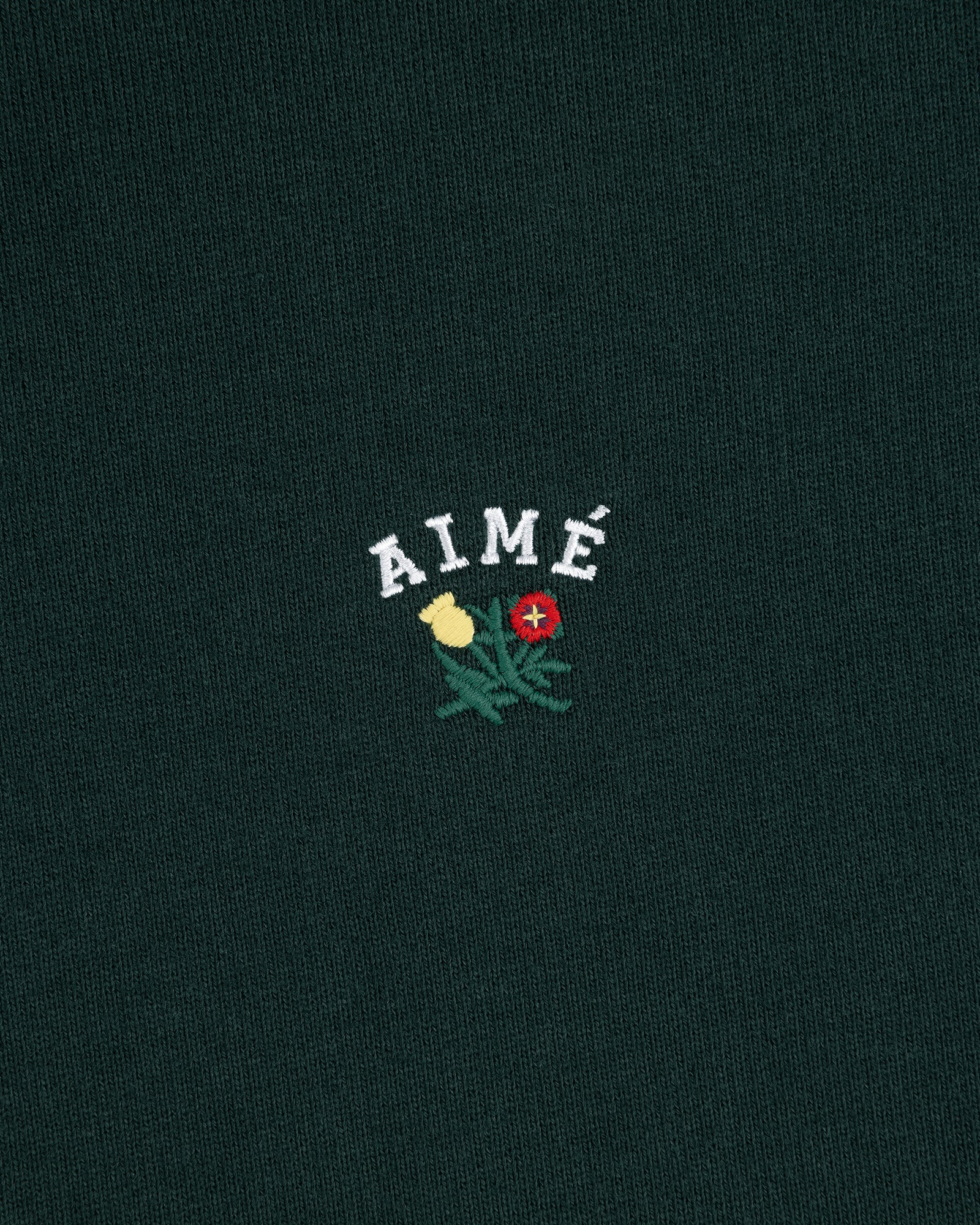 Dark green Crest Quarter Zip Pullover with 'AIMÉ' embroidered above a yellow and a red rose.
