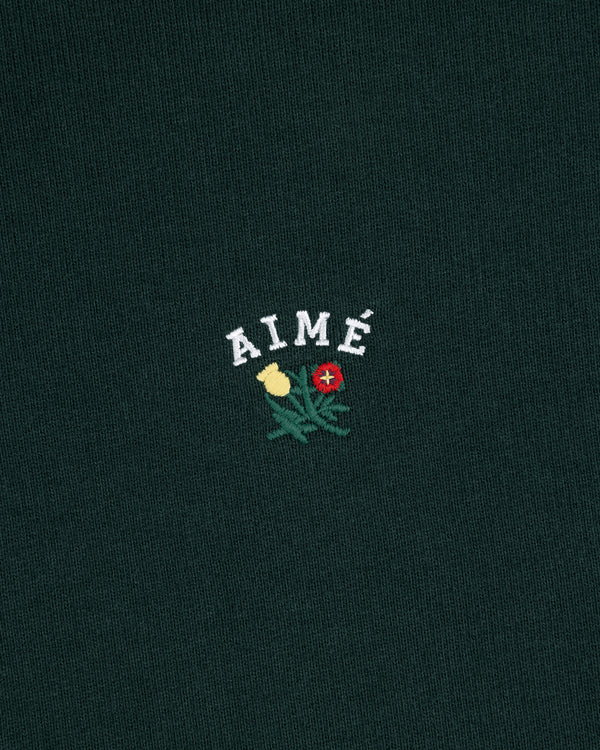 Dark green Crest Quarter Zip Pullover with 'AIMÉ' embroidered above a yellow and a red rose.