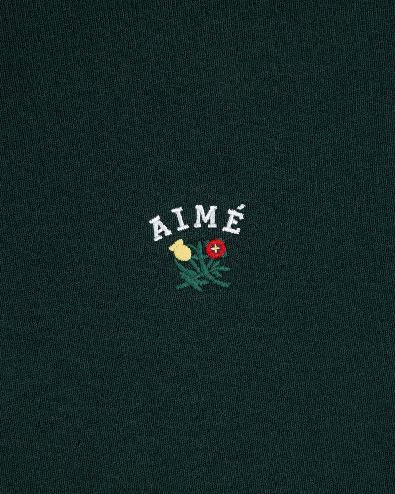 Dark green Crest Quarter Zip Pullover with 'AIMÉ' embroidered above a yellow and a red rose.