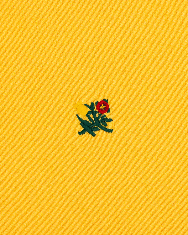 Small red and yellow flower with green leaves embroidered on Sun Faded Crest Quarter Zip’s textured yellow fabric.