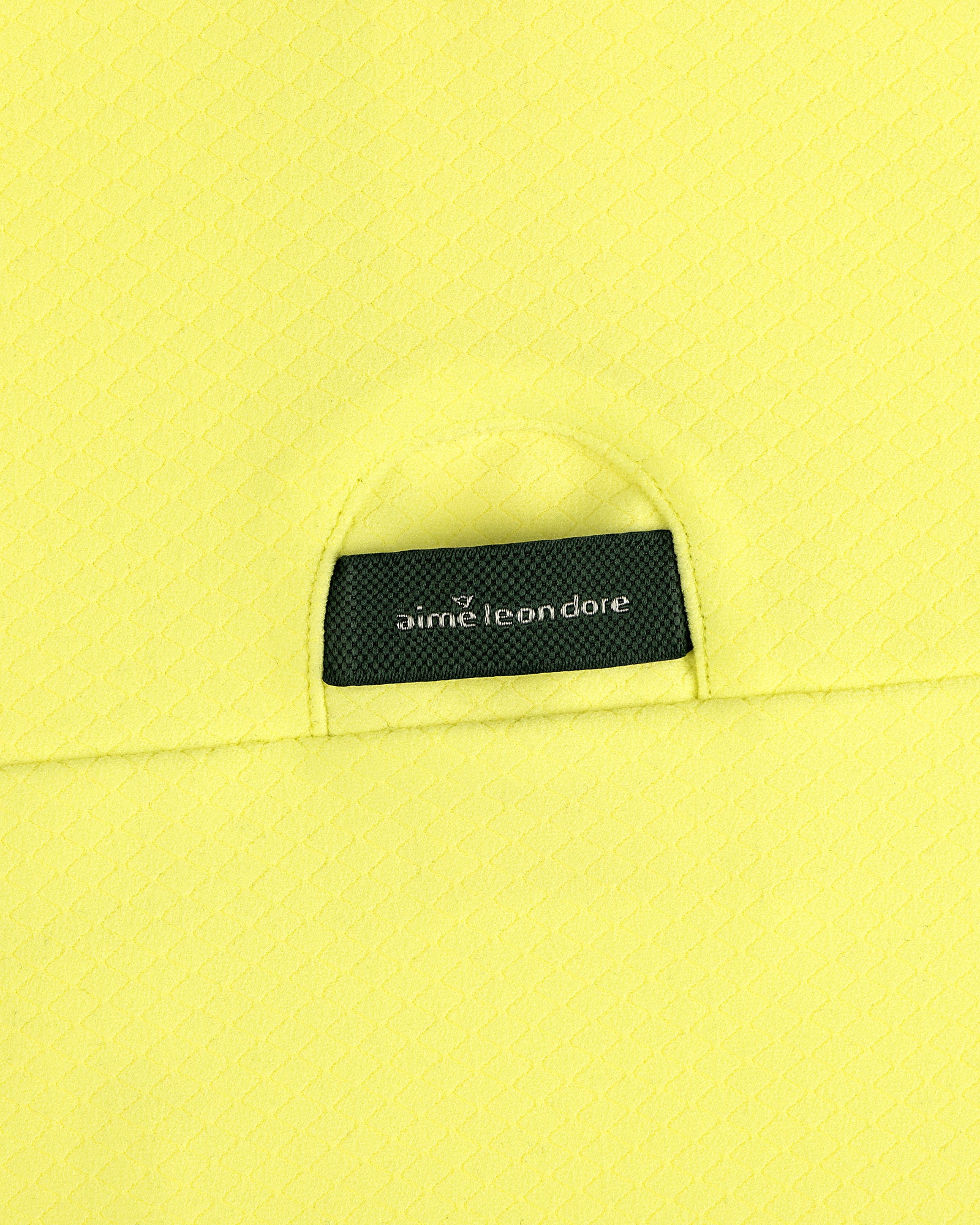 Close-up of yellow ALD Golf Quarter Zip Pullover with a small black aime leon dore label tucked into the pocket.