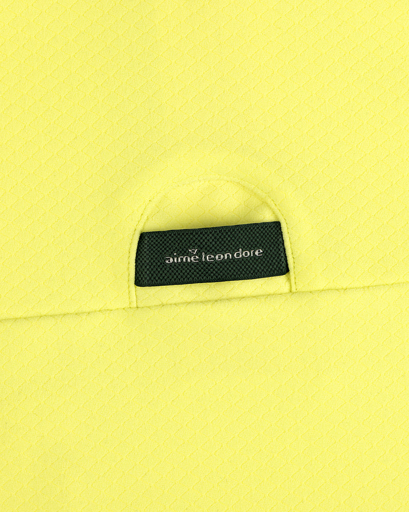 Close-up of yellow ALD Golf Quarter Zip Pullover with a small black aime leon dore label tucked into the pocket.